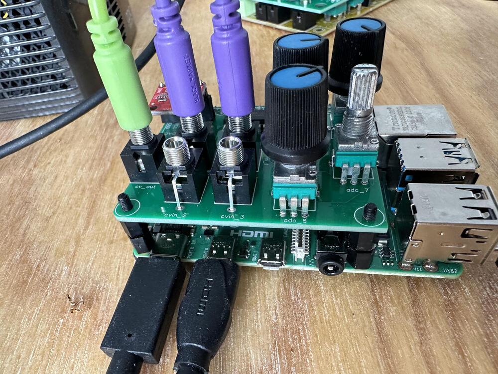 Side shot of RPi with hat. Blue knobs added atop, with two purple 3.5mm cables going into CV in jacks and a green one coming out the CV out jack